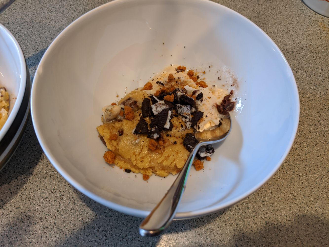 A bowl with half a cookie, a small scoop of ice cream, chunks of gingerbread and some broken up Oreo