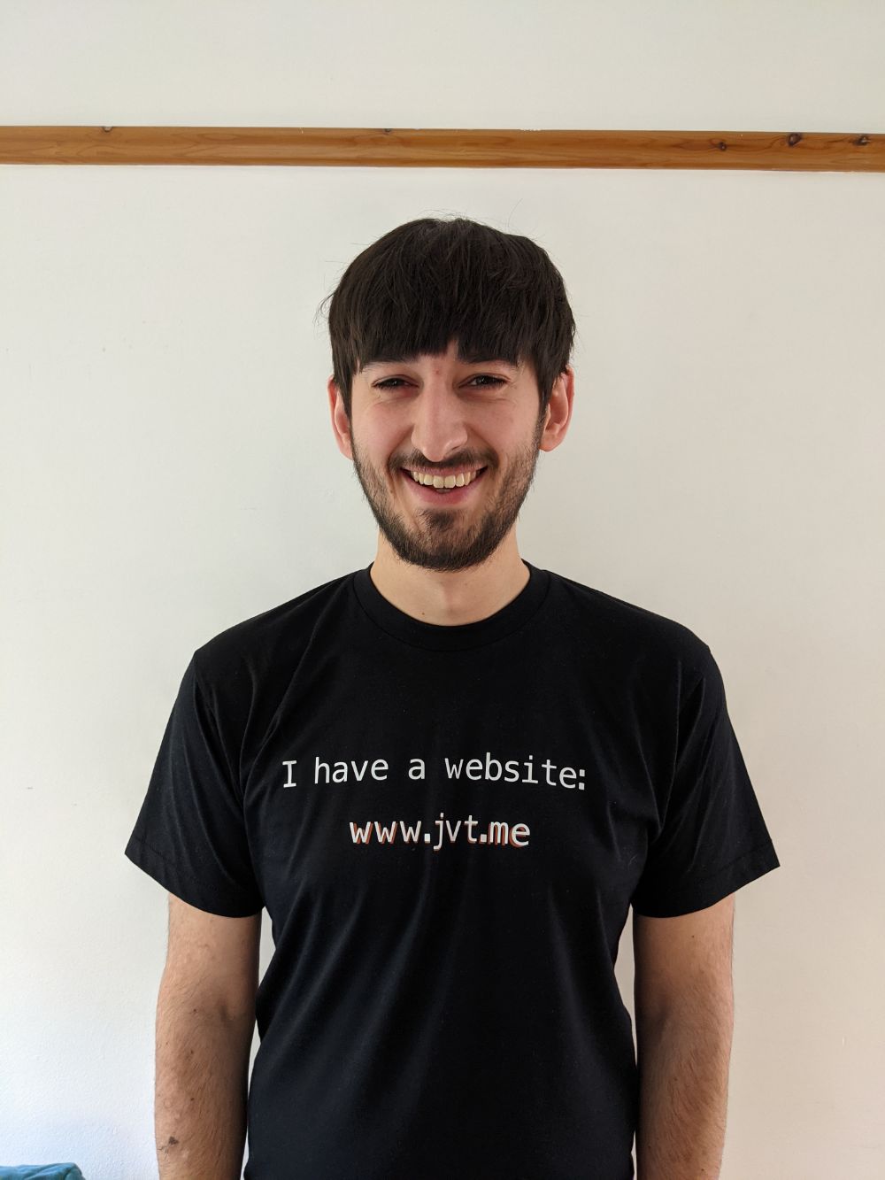 Jamie facing towards the camera, smiling, with "I have a website: www.jvt.me" written on it