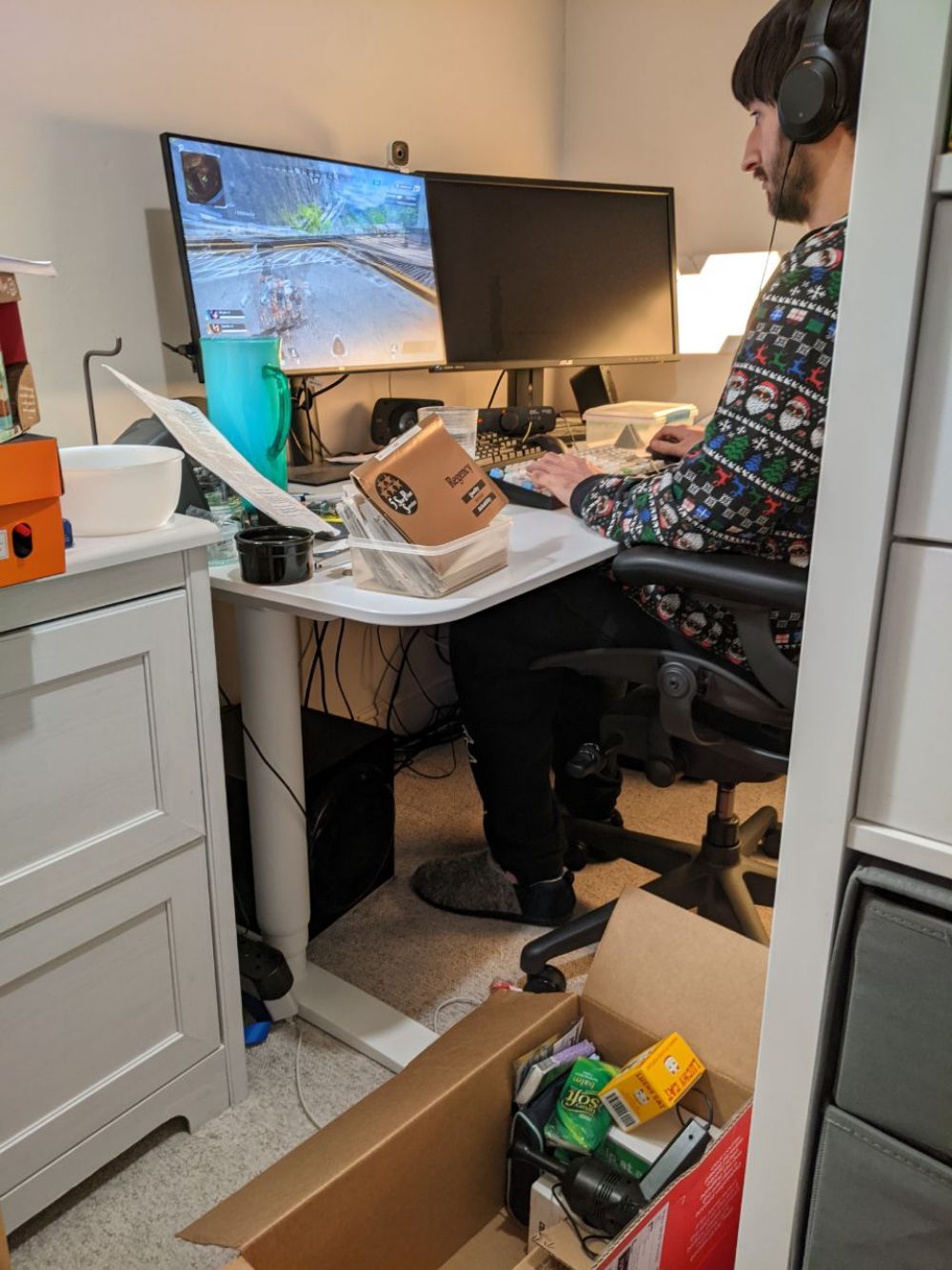 Jamie sitting at his desktop, in a Christmas hoodie, playing Apex Legends while there are boxes and mess everywhere