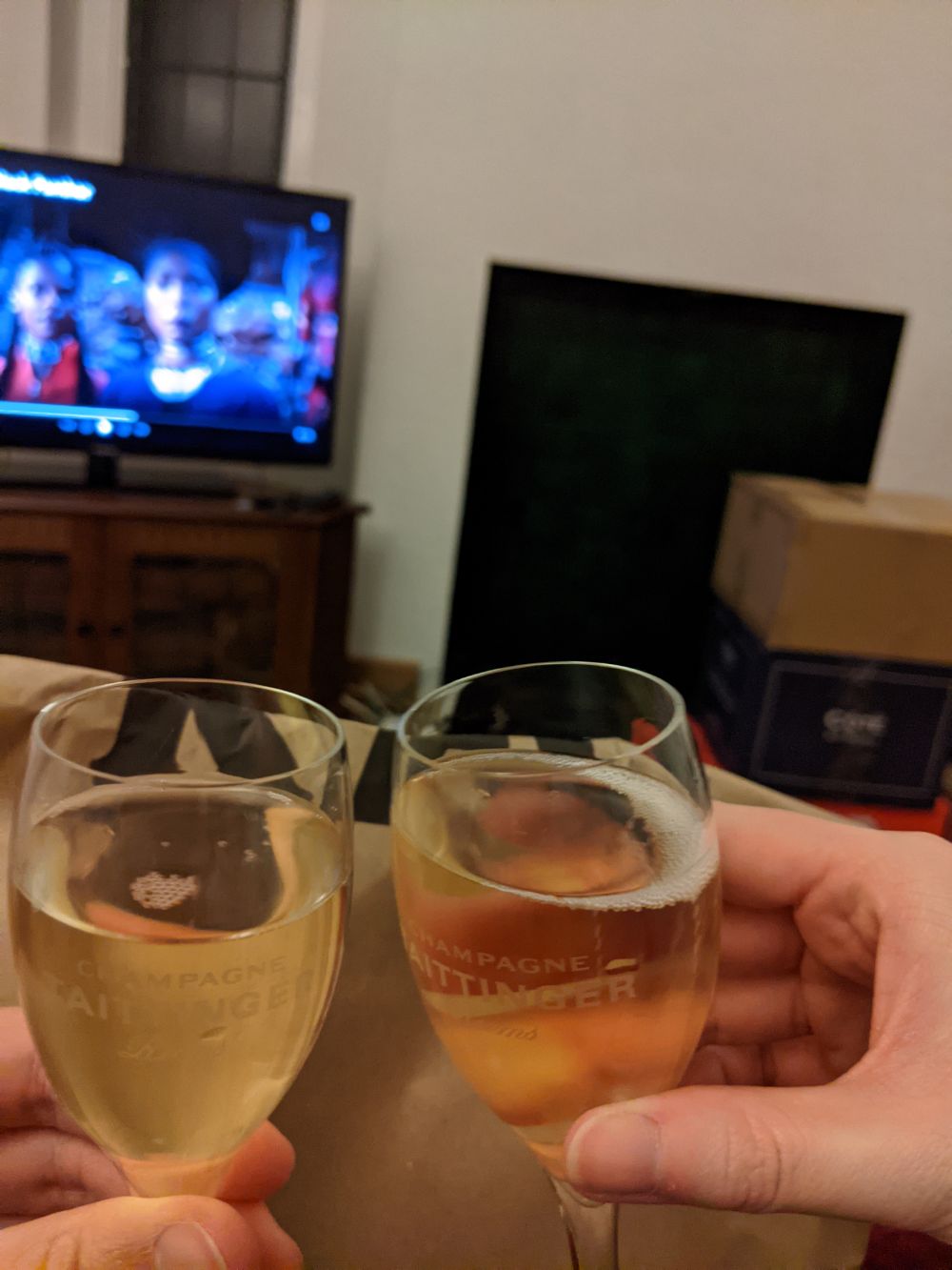 Jamie and Anna toasting to the new house with two Champagne flutes, in front of a bag of KFC, with Black Panther on the TV behind, next to boxes of yet-to-be-unpacked belongings