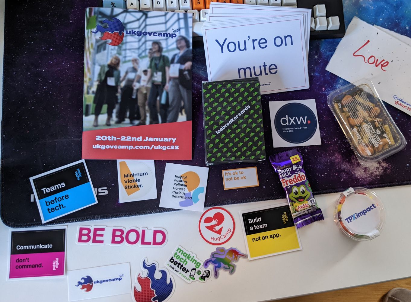 The contents of the swag box laid out, with a dozen stickers, a few snacks, some icebreaker cards, the agenda for the event, cue cards such as "you're on mute"
