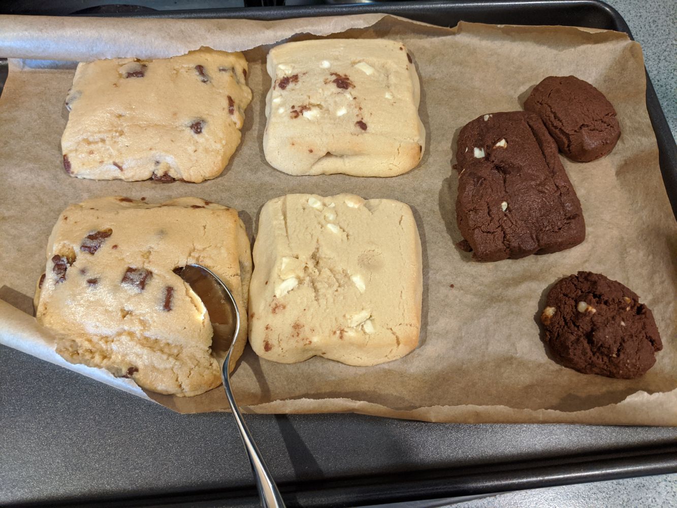 A photo of some somewhat-cooked cookies, with a spoon sinking into one to show how gooey they still are