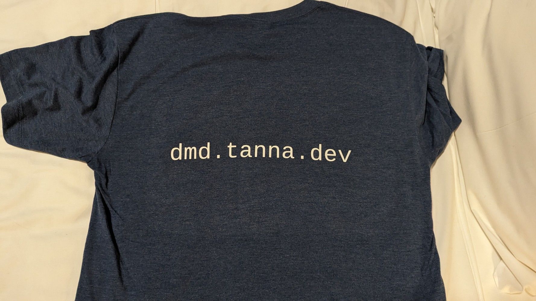 The back of a medium dark blue t-shirt, with the dependency-management-data website, dmd.tanna.dev, printed