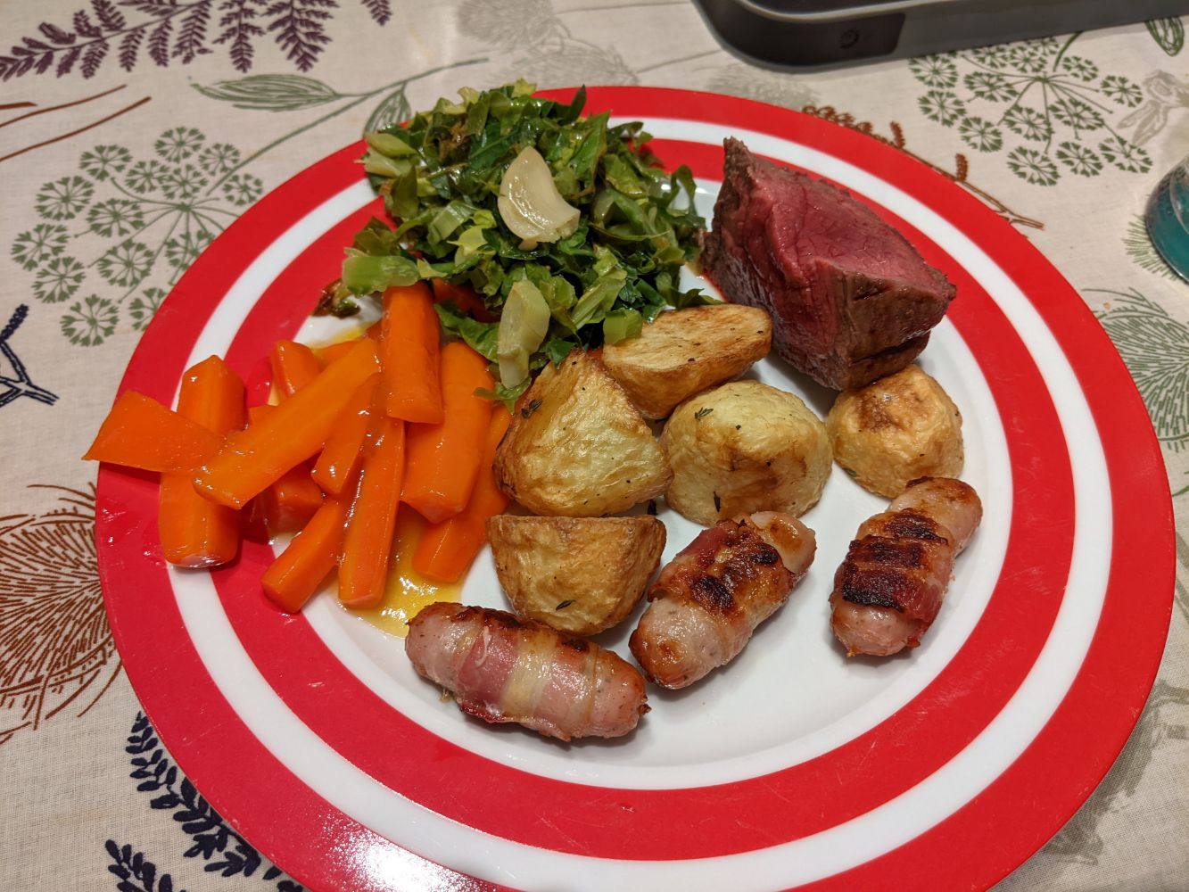 A beef roast with all the trimmings on a plate - marmalade carrots, with a bit of extra marmalade gravy sauce, roast potatoes, spring greens with olive oil and garlic, pigs in blankets, and roast beef that was very rare in the middle 