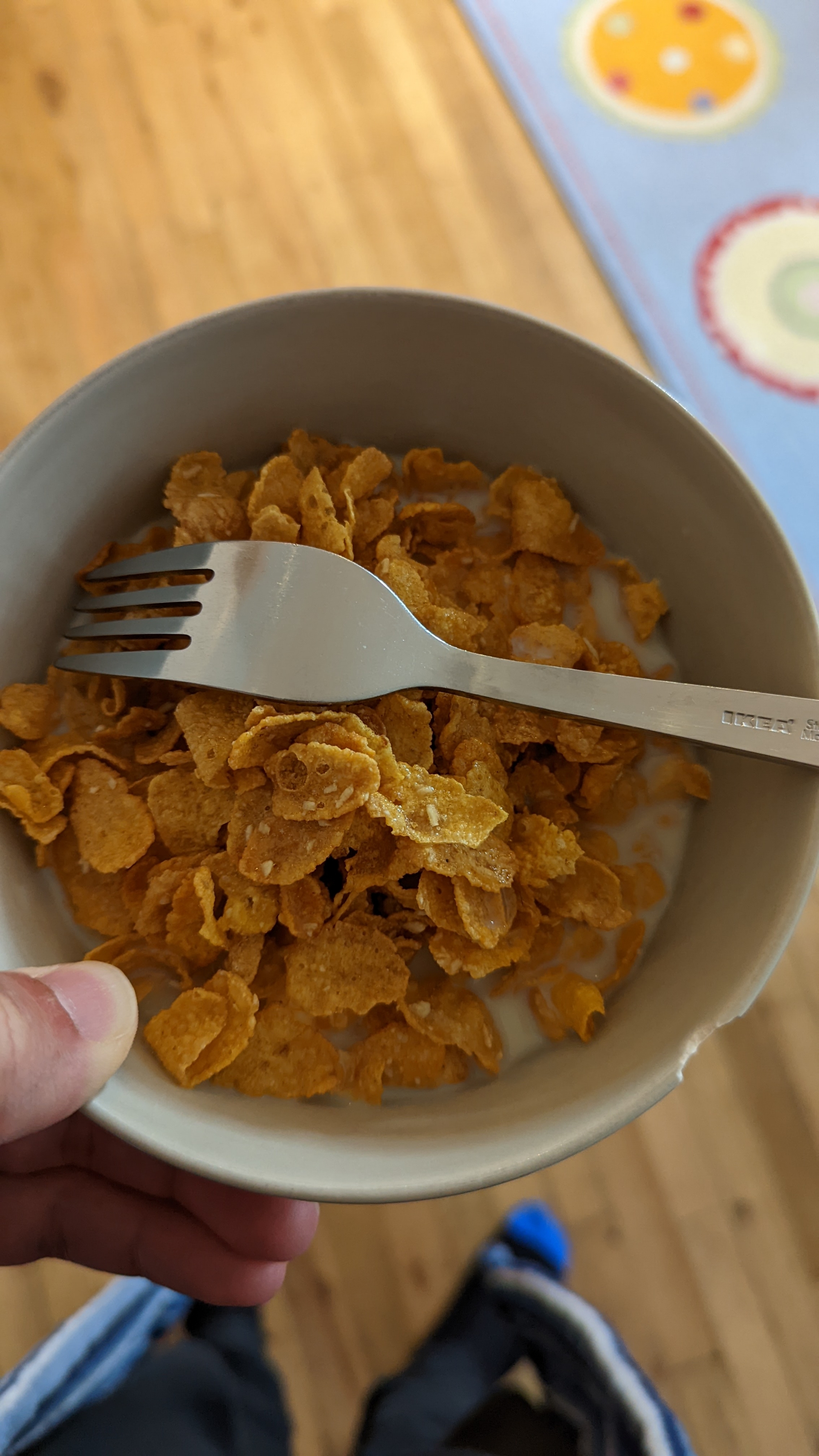 A bowl of cereal, with a fork instead of a spoon, resting on top of it by accident