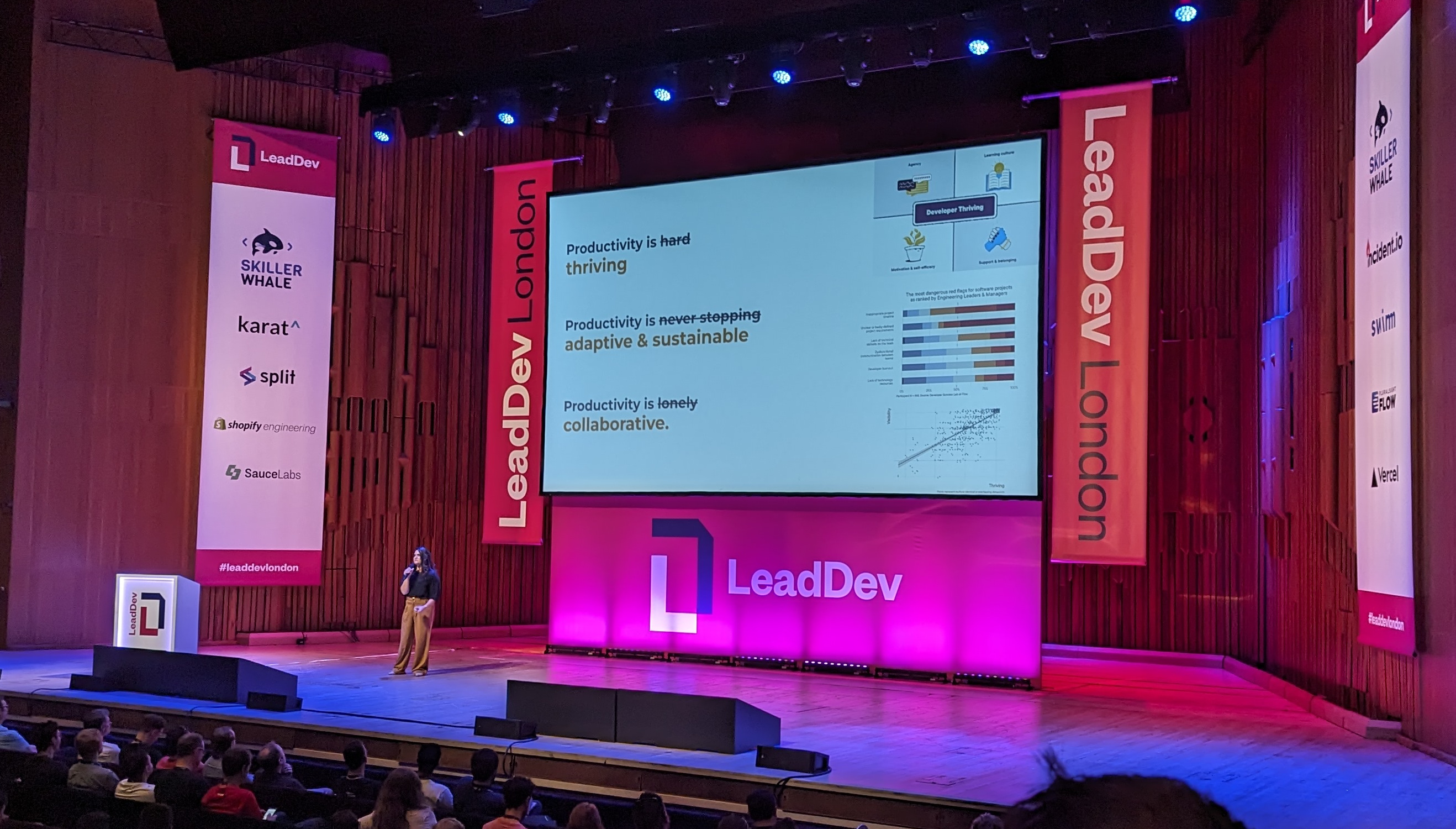 Cat Hicks on the stage at LeadDev in front of a slide with "Productivity is hard (crossed out) thriving", "Productivity is never stopping (crossed out) adaptive and sustainable", "Productivity is lonely (crossed out) collaborative"