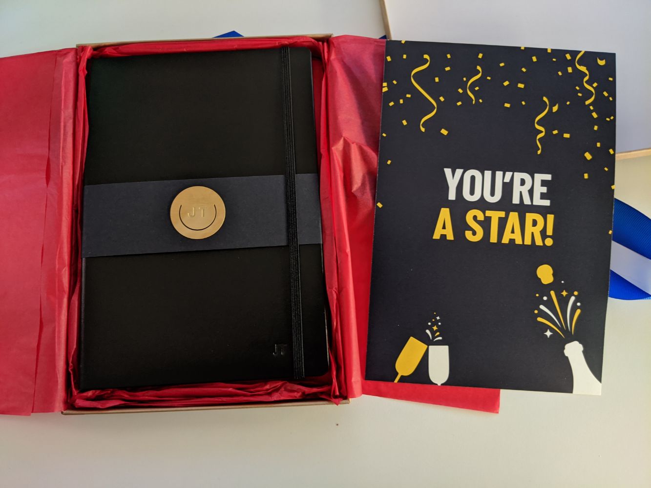 The inside of the parcel - on the right, a card with celebratory images, and "You're a star!" on it. On the left, a black notebook, embossed with Jamie's initials