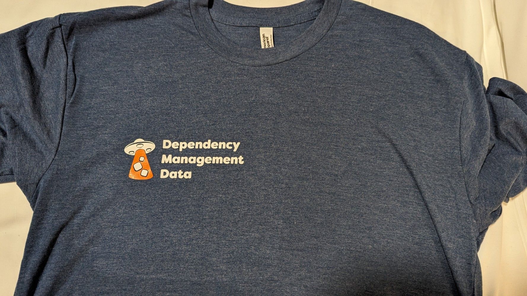 The front of a medium dark blue t-shirt, with the dependency-management-data logo over the right hand breast