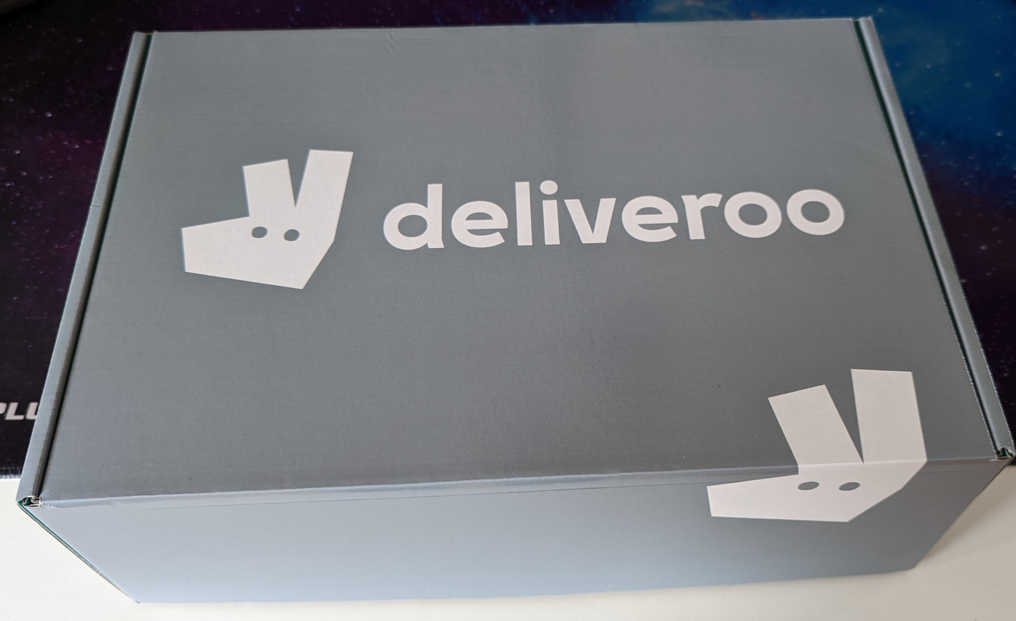 A box with the Deliveroo name and logo on it, in the Deliveroo grey