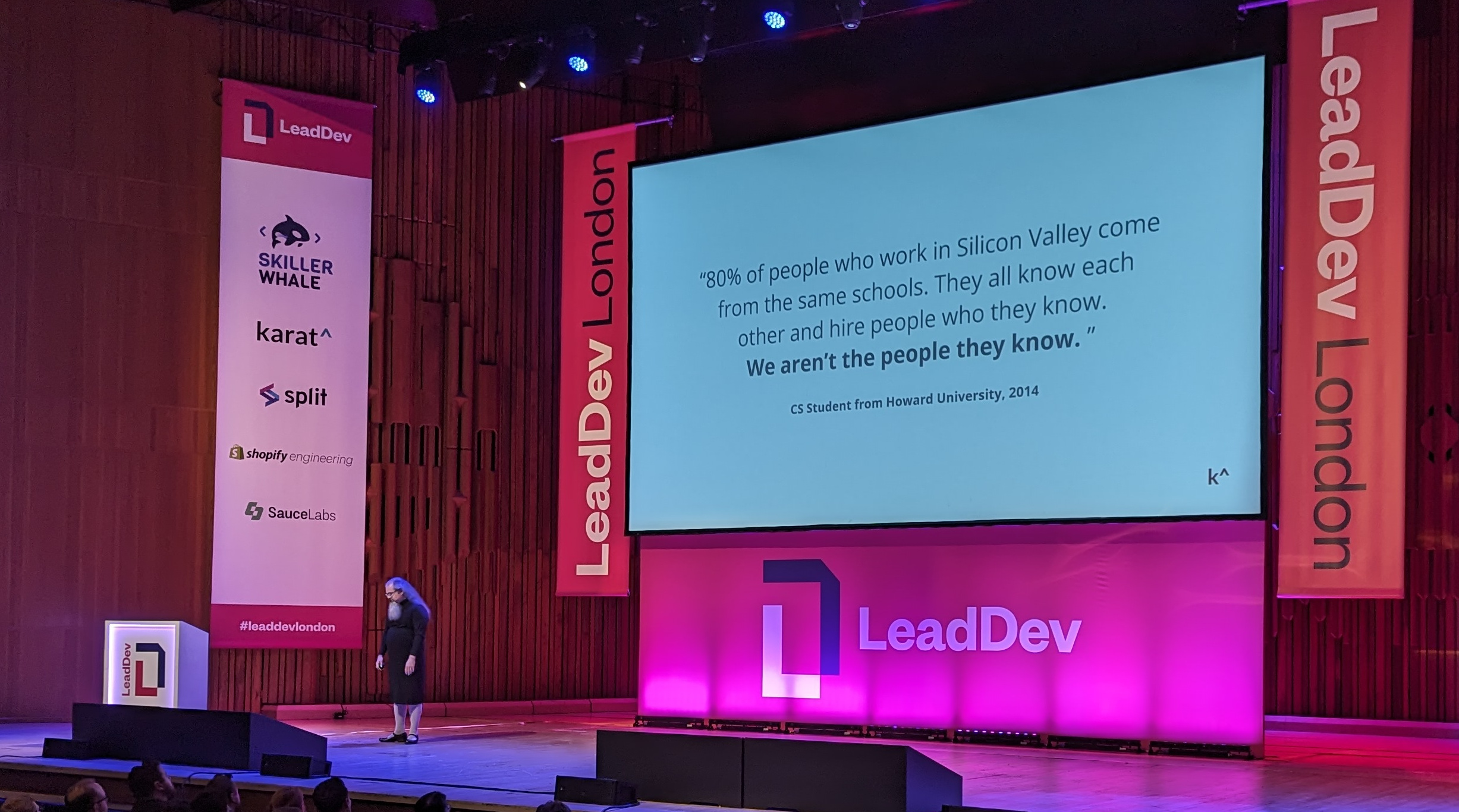Jason standing on the stage at LeadDev London, in front of a slide with a quote by a CS Student from Howard University from 2014, "80% of the people who work in Silicon Valley come from the same schools. They all know each other and hire people who they know. We aren't the people they know"