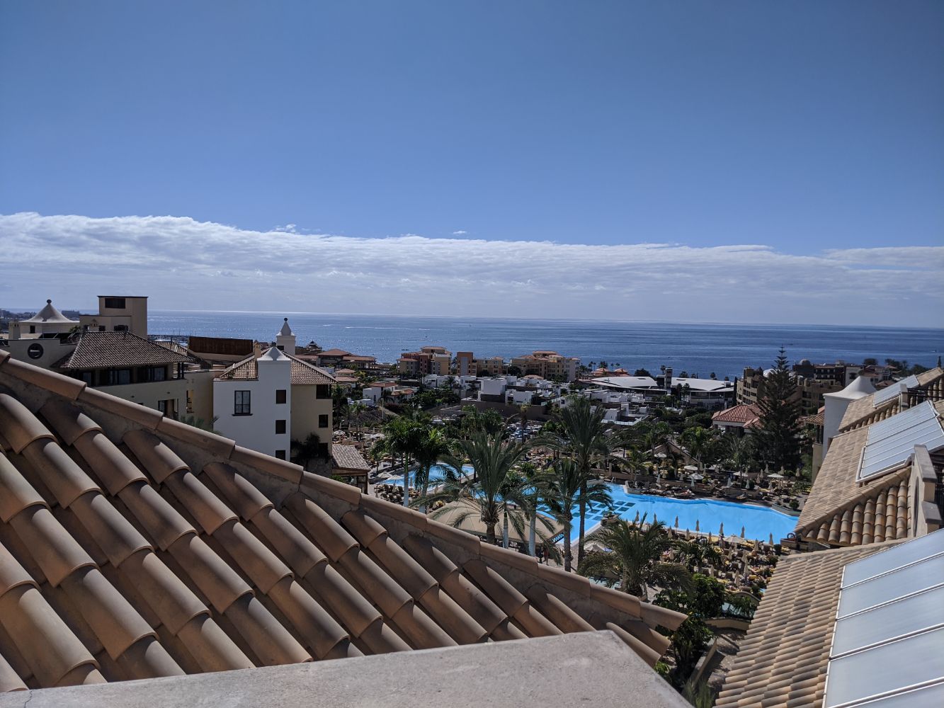 A sunny day looking out from the roof over the pool, buildings and the sea, with a few clouds in the sky A sunny day looking out from the roof over the pool, buildings and the sea, with a few clouds in the sky