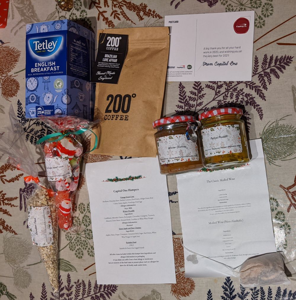 A box of Tetley English Breakfast tea, a carton of 200 Degrees Brazillian Love Affair coffee, a card from Capital One, a cone titled reindeer food and a warning that it isn't for human consumption, a cone of sweets, a jar of winter chutney, a jar of festive picallili, and a mulled wine kit with instructions for alcoholic and non-alcoholic variants