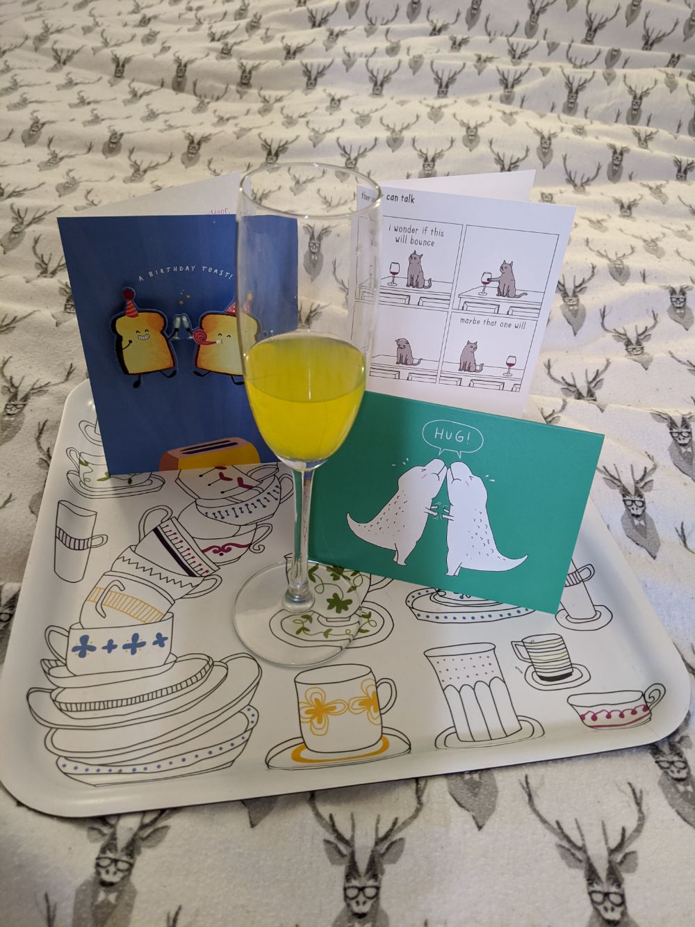 Three birthday cards on a tray, circling a champagne flute that looks like it is full of bucks fizz but is actually Tango