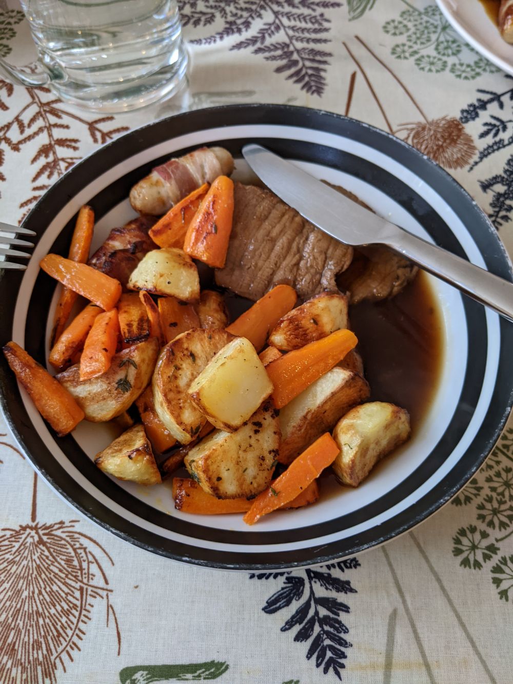A dish filled with a roast beef dinner - air fryer cooked carrots, roast potatoes and roast beef, with pigs in blankets and gravy