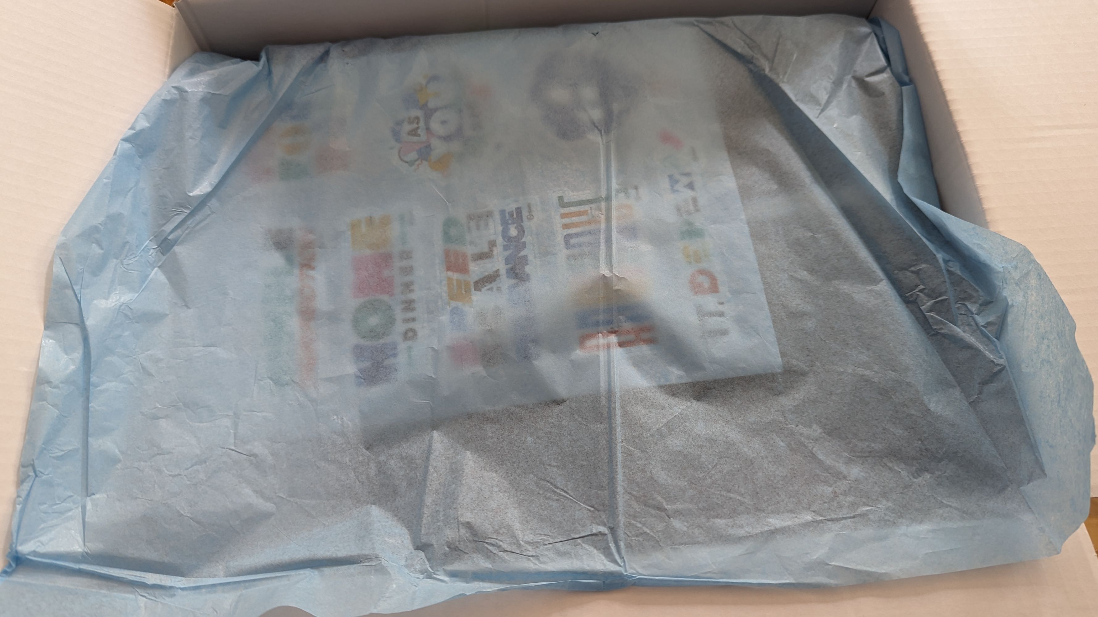 A box of swag, covered with a light blue piece of tissue paper, teasingly not quite showing what is in the box