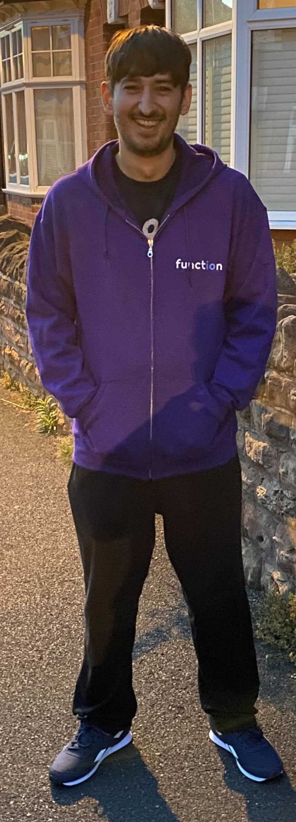 Jamie standing in the street, with his new bright purple Project Function hoodie on, smiling
